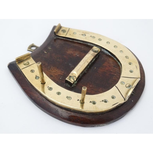 389 - A small brass cribbage board formed as a horseshoe, with two pegs and mounted upon a wooden plinth. ... 