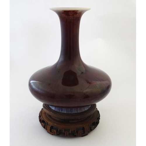 403 - A Chinese Sang de Boeuf flared rim bottle vase on carved wooden stand. 9 1/2'' high.