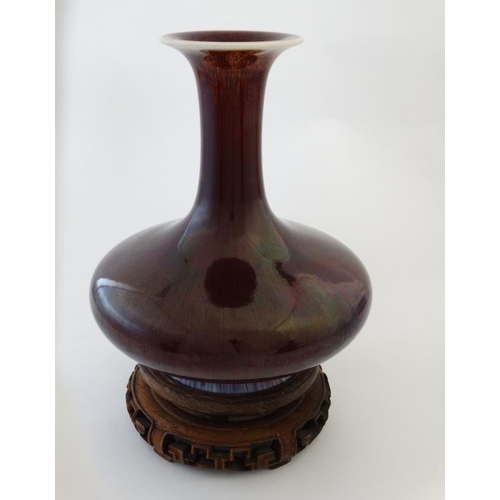 403 - A Chinese Sang de Boeuf flared rim bottle vase on carved wooden stand. 9 1/2'' high.