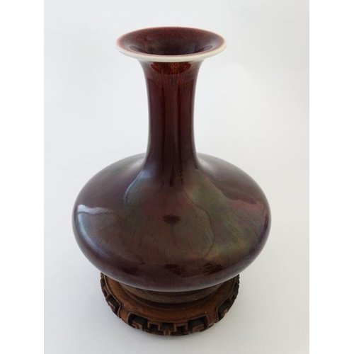 403 - A Chinese Sang de Boeuf flared rim bottle vase on carved wooden stand. 9 1/2'' high.