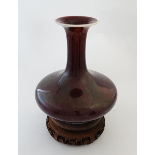 403 - A Chinese Sang de Boeuf flared rim bottle vase on carved wooden stand. 9 1/2'' high.