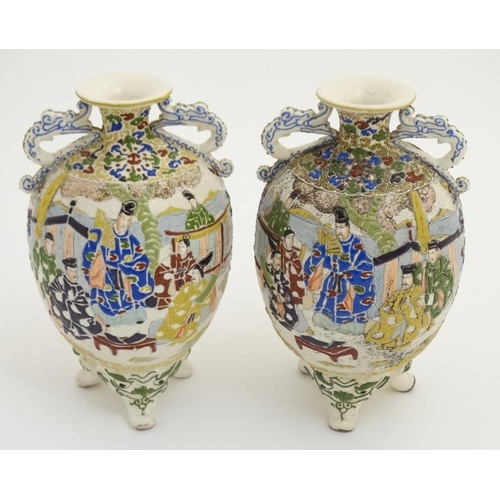 430 - A pair of Japanese Satsuma Moriage twin handled vases on tripod feet, each decorated in polychrome w... 