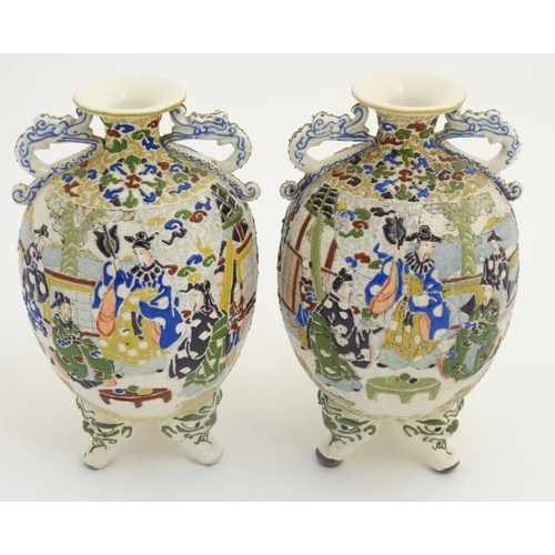 430 - A pair of Japanese Satsuma Moriage twin handled vases on tripod feet, each decorated in polychrome w... 