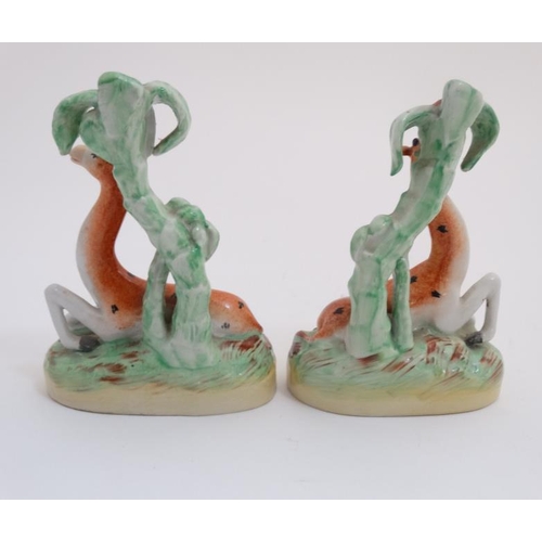 450 - A pair of 19thC handed Staffordshire Giraffe figures lying under palm trees, decorated in shades of ... 