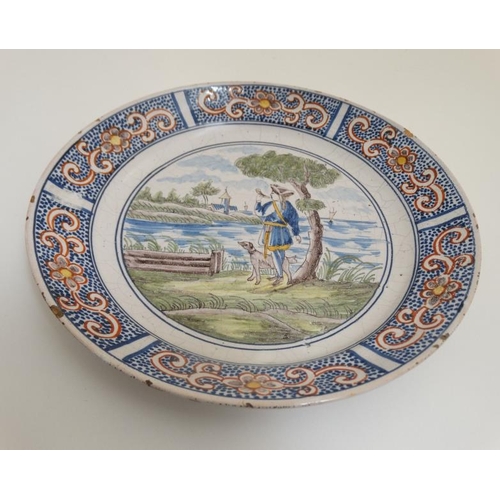 455 - An early 19thC Dutch Delft plate , decorated with figure and dog beside the sea with building in the... 