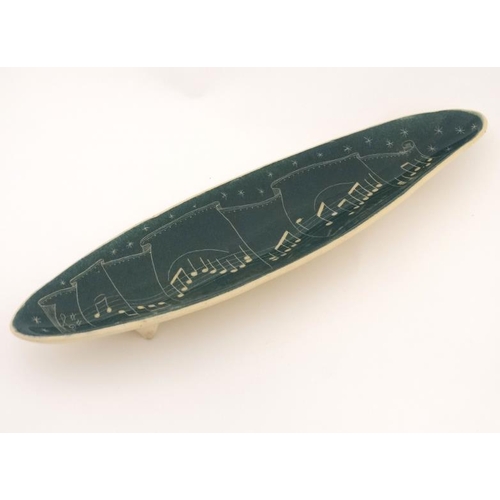 480 - An elongated ceramic dish decorated with musical notes in cream on a green ground. 16'' long.