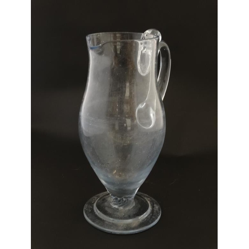 646 - A tall clear glass pedestal jug with loop handle 11'' high