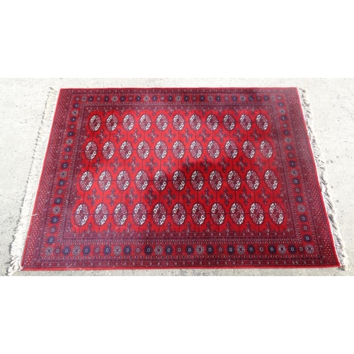 77 - Rug / Carpet :   A woollen Bokara Rug with wine red ground and 4 x 11 (44) botehs to center ,  99 x ... 