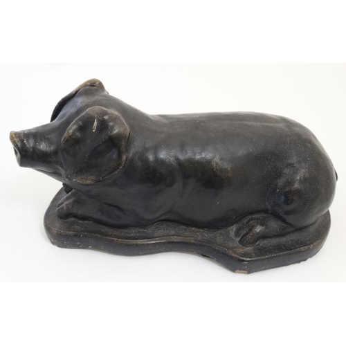 891 - A mid / late 20thC black painted reconstituted stone model of a recumbent pig 19 1/2'' long x 9 1/4'... 