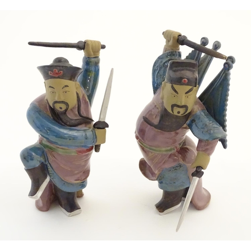 23 - Two Oriental ceramic figures posed in combat with a lustre glaze, each holding two swords, one with ... 