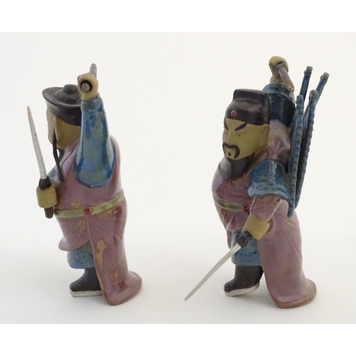 23 - Two Oriental ceramic figures posed in combat with a lustre glaze, each holding two swords, one with ... 