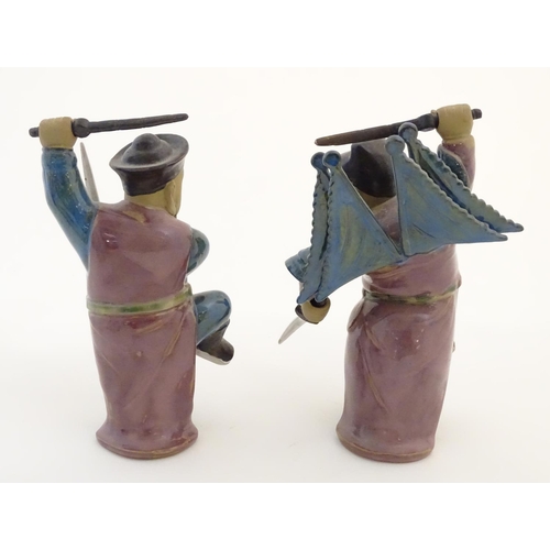 23 - Two Oriental ceramic figures posed in combat with a lustre glaze, each holding two swords, one with ... 