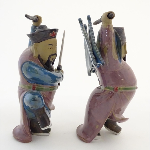 23 - Two Oriental ceramic figures posed in combat with a lustre glaze, each holding two swords, one with ... 