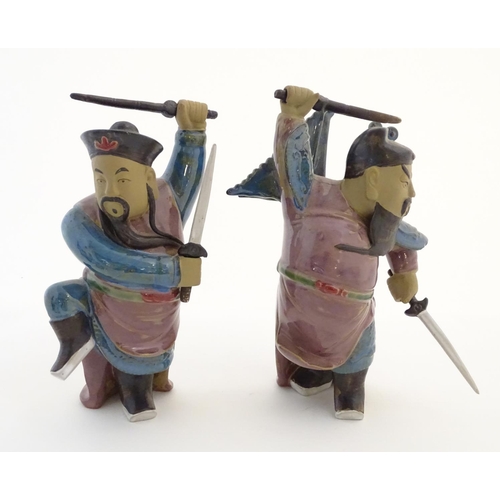 23 - Two Oriental ceramic figures posed in combat with a lustre glaze, each holding two swords, one with ... 