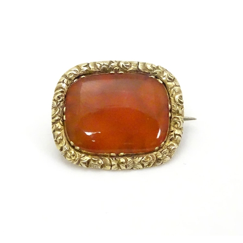 303 - A 19thC brooch set with central carnelian within an engraved yellow metal mount. 3/4'' wide