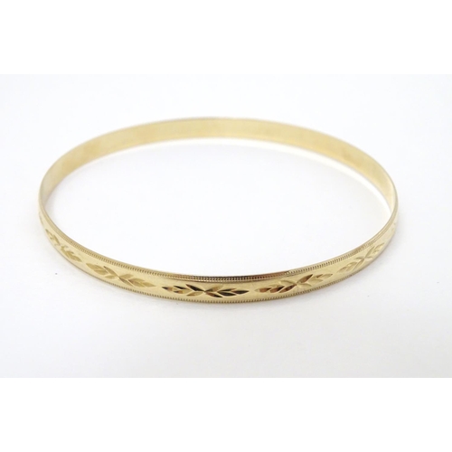 325 - A 9ct gold bangle bracelet with engraved decoration (7.1g)