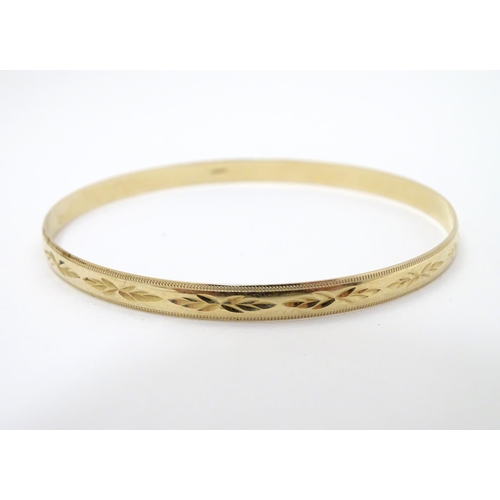 325 - A 9ct gold bangle bracelet with engraved decoration (7.1g)