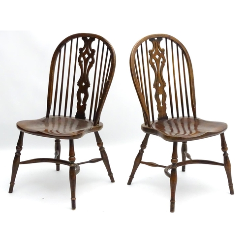 273 - A pair of early 20thC Windsor chairs with a wheelback and pierced central splat above a saddle seat ... 