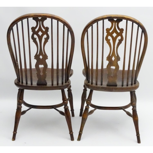 273 - A pair of early 20thC Windsor chairs with a wheelback and pierced central splat above a saddle seat ... 