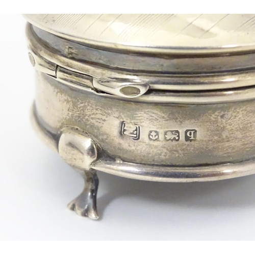 178 - A silver ring box with engine turned decoration and standing on three feet. Hallmarked Birmingham 19... 