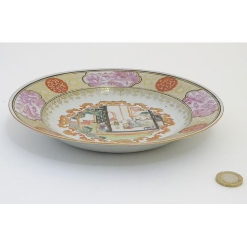 52 - A Chinese plate with a central panel depicting an interior scene with figures and a garden, with gil... 