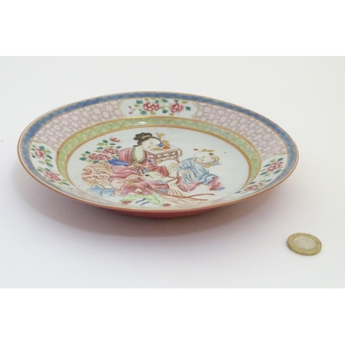 53 - A Chinese famille rose plate decorated with three figures in an interior, with a vase of flowers and... 