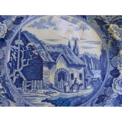 65 - A 19thC blue and white transferware plate depicting a country scene with a thatched cottage, figures... 