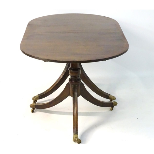 183 - An early 20thC mahogany Regency style dining table, with splayed fluted sabre legs terminating in br... 