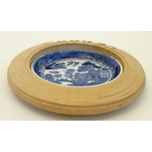 242 - A blue and white ceramic 'Willow' pattern butter dish in carved wooden surround. 6'' diameter.