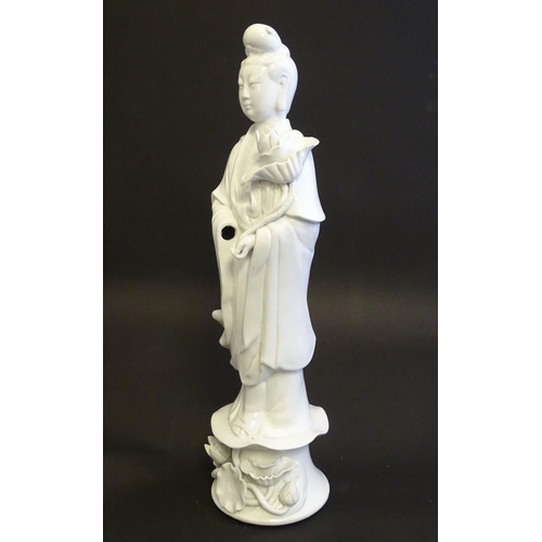 19 - A Chinese blanc de chine figure of Guanyin standing holding flowers, raised on a base of lotus flowe... 