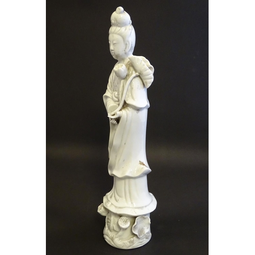 8 - A Chinese blanc de chine figure of Guanyin holding flowers, raised on a base of lotus flowers and li... 