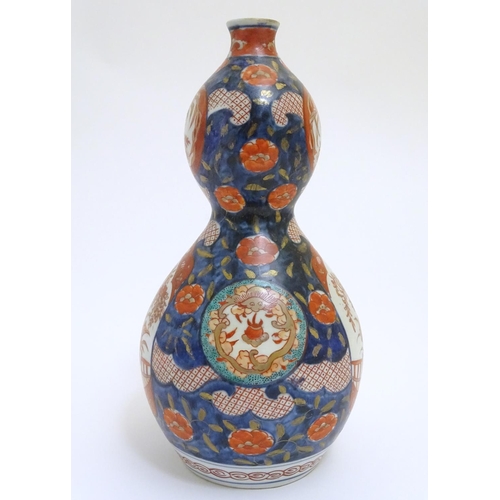 30 - An Oriental double gourd vase in the Imari palette with lobed panels depicting plants on a terrace, ... 