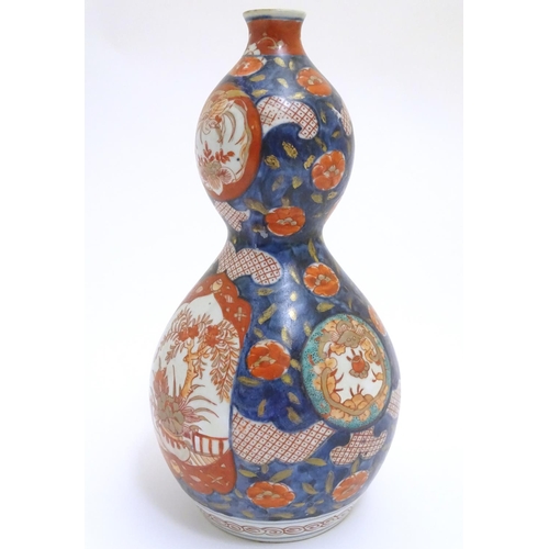 30 - An Oriental double gourd vase in the Imari palette with lobed panels depicting plants on a terrace, ... 