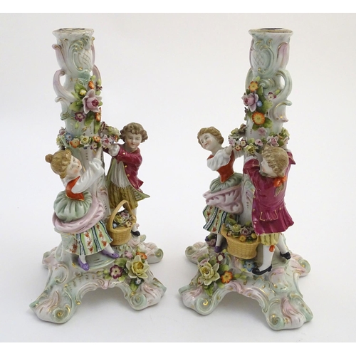 73 - A pair of 19thC German figural lamp bases with two figures arranging flowers, raised on a scrolling ... 