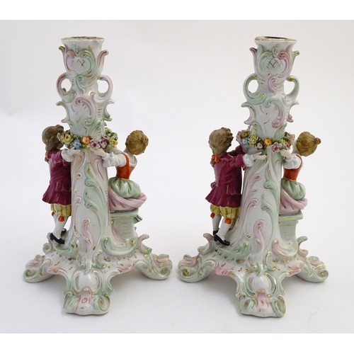 73 - A pair of 19thC German figural lamp bases with two figures arranging flowers, raised on a scrolling ... 