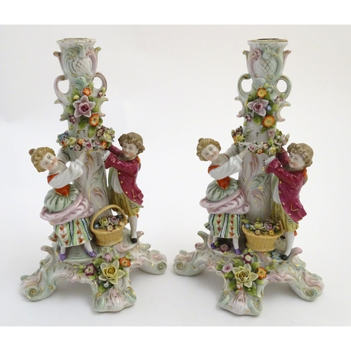 73 - A pair of 19thC German figural lamp bases with two figures arranging flowers, raised on a scrolling ... 