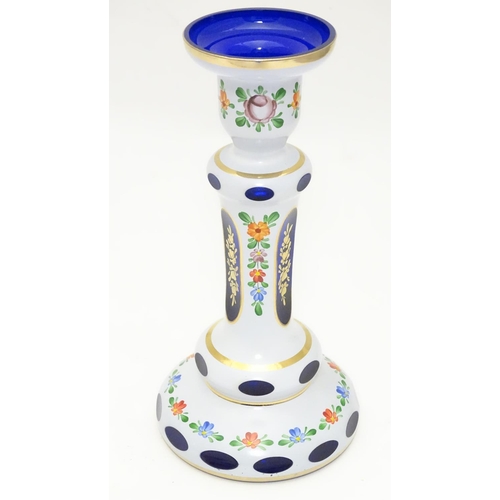 154 - An early 20thC Bohemian blue glass candlestick, overlaid with white base, gilt banding and floral mo... 