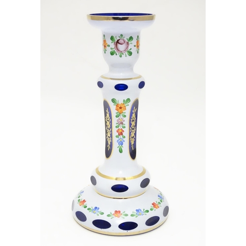 154 - An early 20thC Bohemian blue glass candlestick, overlaid with white base, gilt banding and floral mo... 