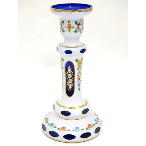 154 - An early 20thC Bohemian blue glass candlestick, overlaid with white base, gilt banding and floral mo... 