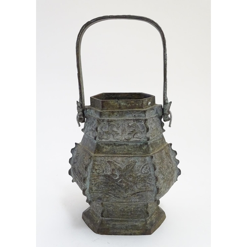 833 - An Oriental cast baluster vase of hexagonal form with a swing handle, the body decorated with panels... 