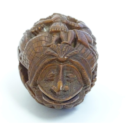 836 - A Continental carved nut snuff bottle with two stylised faces to each end, the body carved with stac... 