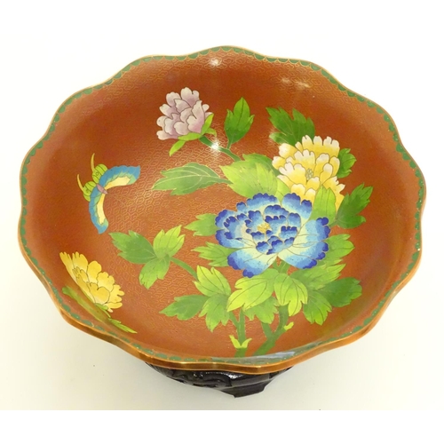 852 - A Chinese cloisonne ware bowl with a lobed rim, decorated with flowers and butterflies, on a carved ... 