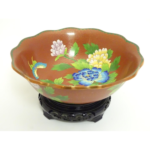 852 - A Chinese cloisonne ware bowl with a lobed rim, decorated with flowers and butterflies, on a carved ... 