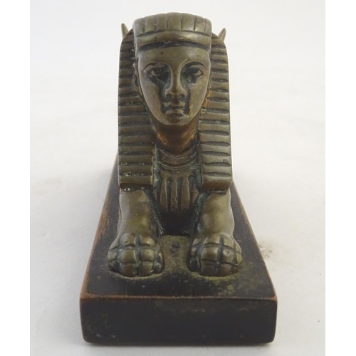 969 - A 20thC paperweight formed as a winged sphinx with the head of a pharaoh on a rectangular wooden bas... 