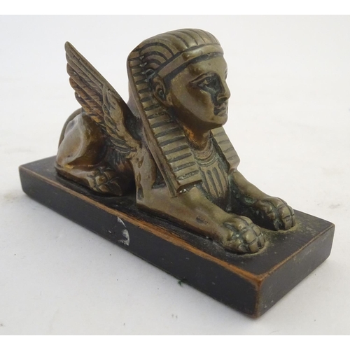 969 - A 20thC paperweight formed as a winged sphinx with the head of a pharaoh on a rectangular wooden bas... 