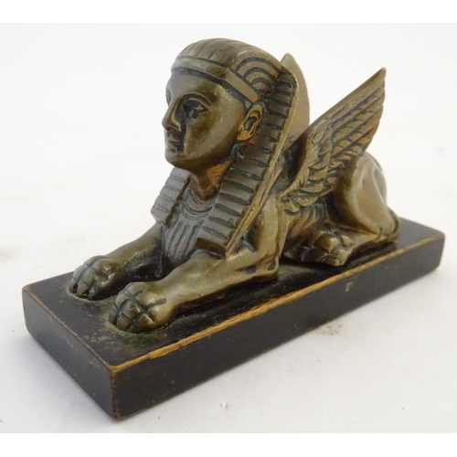 969 - A 20thC paperweight formed as a winged sphinx with the head of a pharaoh on a rectangular wooden bas... 