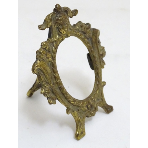 987 - A late 19th /early 20thC cast brass easel back oval frame with floral and scroll detail, surmounted ... 