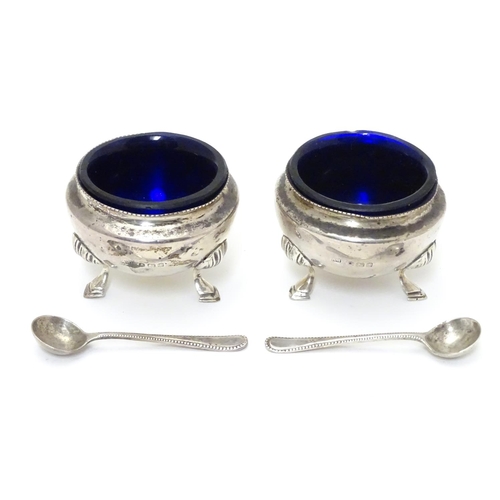 312 - A pair of circular silver table salts, each raised on three hoof feet, with blue glass liners and ma... 