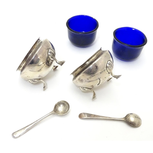 312 - A pair of circular silver table salts, each raised on three hoof feet, with blue glass liners and ma... 