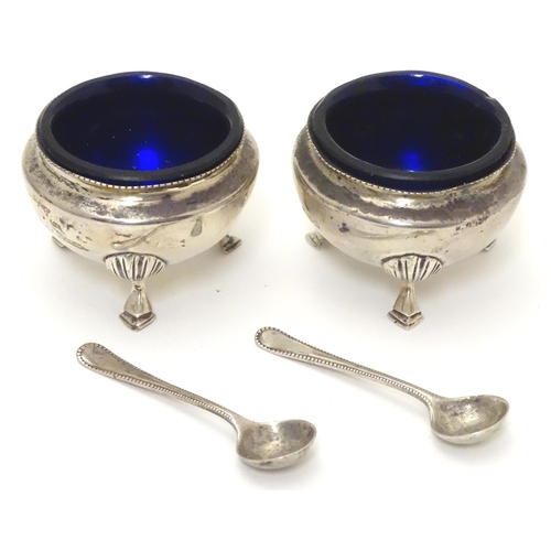 312 - A pair of circular silver table salts, each raised on three hoof feet, with blue glass liners and ma... 